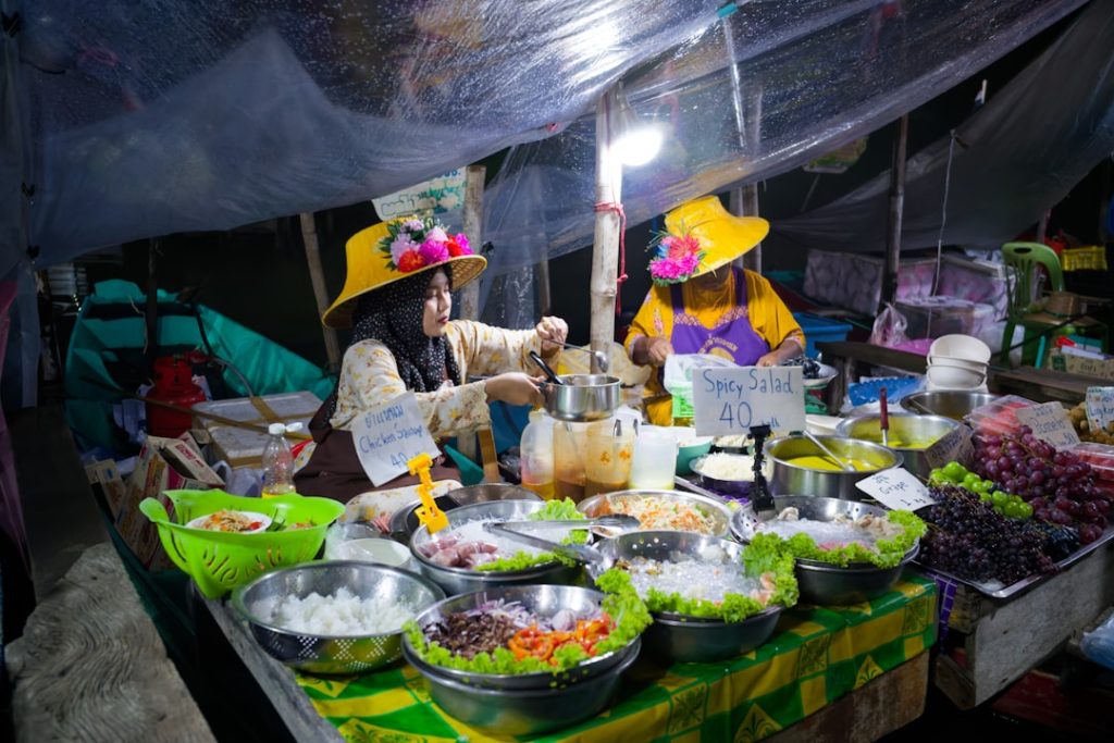 two-women-in-yellow-hats-serve-food-at-a-stall-npgi9wbuh8u
